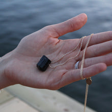 Load image into Gallery viewer, Woman holding our Black tourmaline necklace with 80 cm long chain in her hands. Details in 18k gold plated sterling silver. Ocean background.
