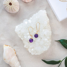 Load image into Gallery viewer, Elegant Amethyst earrings with details in 18k gold-plated 925 sterling silver. Presented on a crystal cluster on a beach

